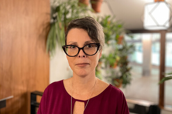 Paula Nixon looking at the camera, in an indoor space with a plant in the background.