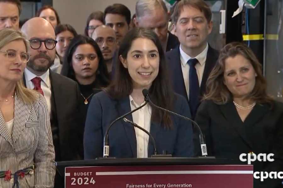 a woman speaking at a podium with a crowd behind her