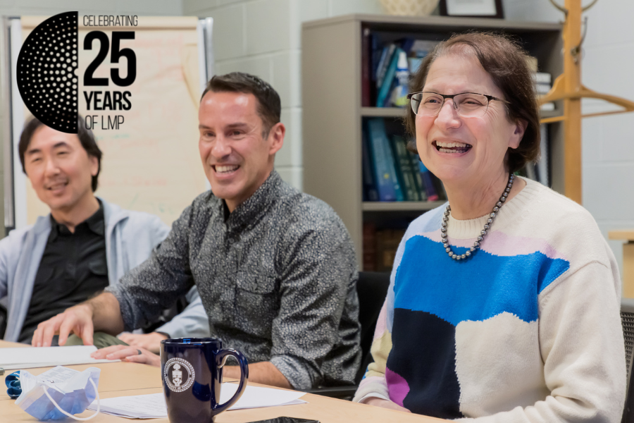 A woman and two men smiling as they talk around a table