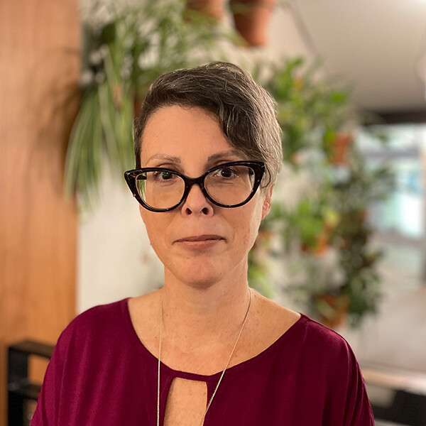 Paula Nixon looking at the camera, in an indoor space with a plant in the background.